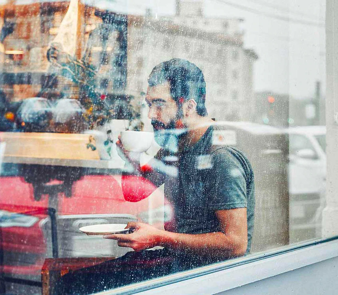 Man sitting in rainy window drinking Pavement Coffee